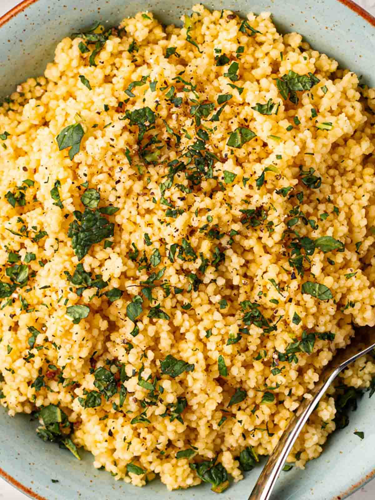 A close up of a bowl of couscous with chopped mint and a fork.