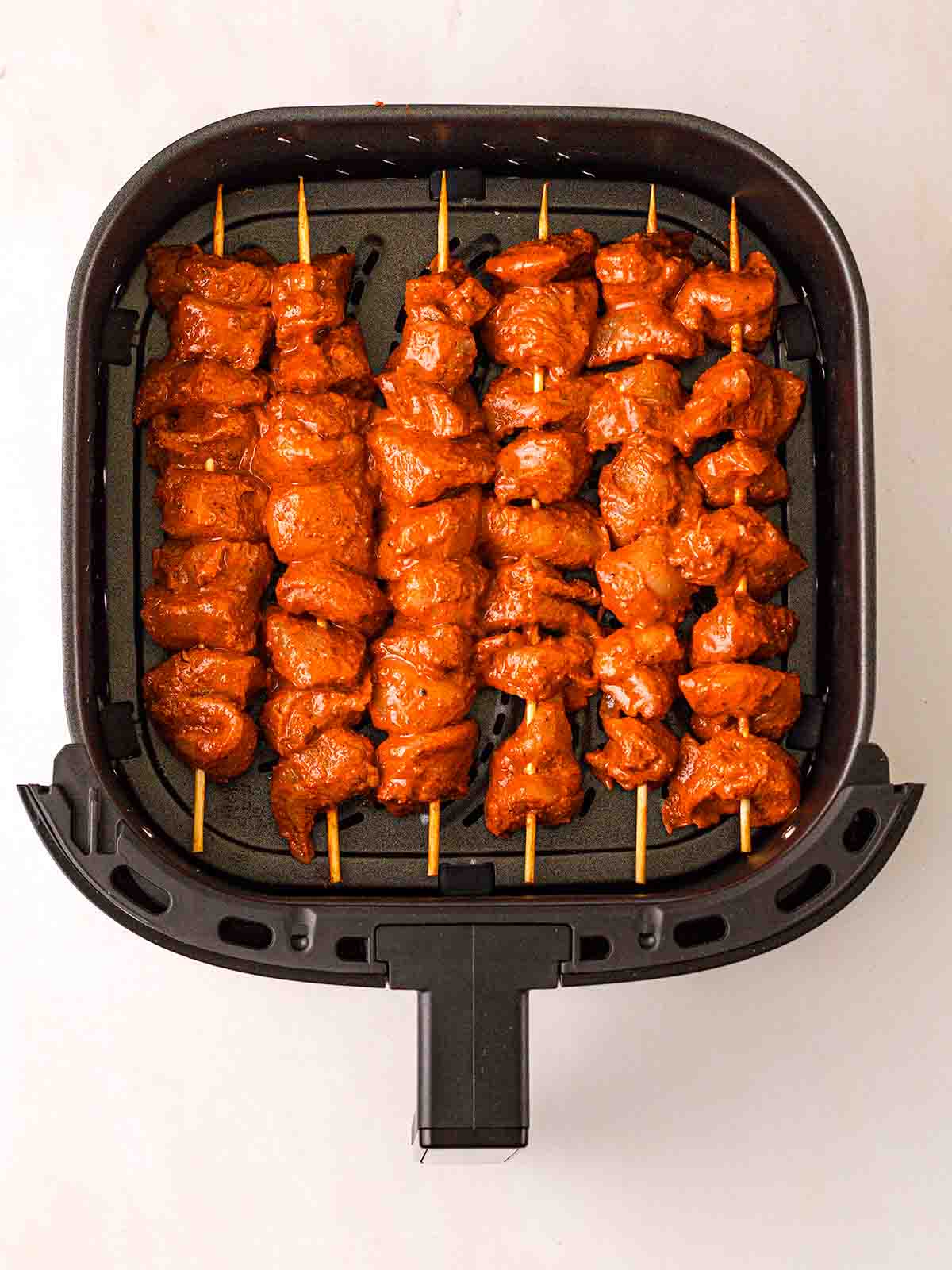 An air fryer tray from above with rows of tandoor chicken on skewers.